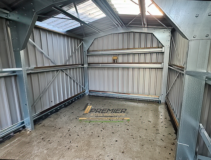 The empty interior of a small steel shed showing the galvanized frame, wall girts, and internal cross-bracing.