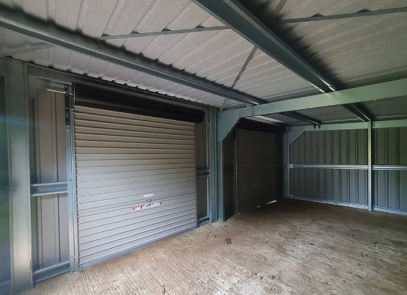 Interior view of a galvanized steel building frame featuring corrugated roofing and two grey roller shutter doors.