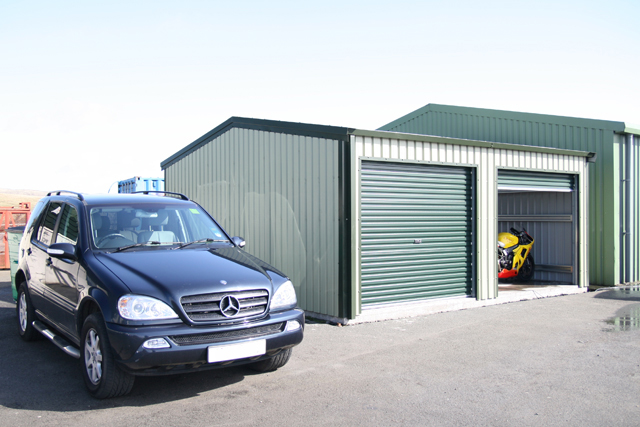 A 4x4 car beside a green building with one roller door open and the other closed