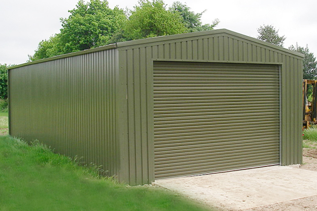 A large dark green building with paving beside lush green grass