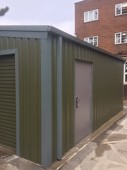 Close-up corner view of a green metal building showing the detail of the side personnel door and the ribbed cladding.